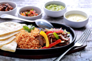 fajitas de res mexicanas servidas con arroz, tortillas de harina suaves en un plato caliente y cuatro salsas diferentes
