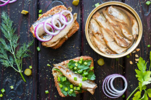 pan de grano con sardinas y verduras junto a los espadines del banco sobre un fondo negro con eneldo y perejil